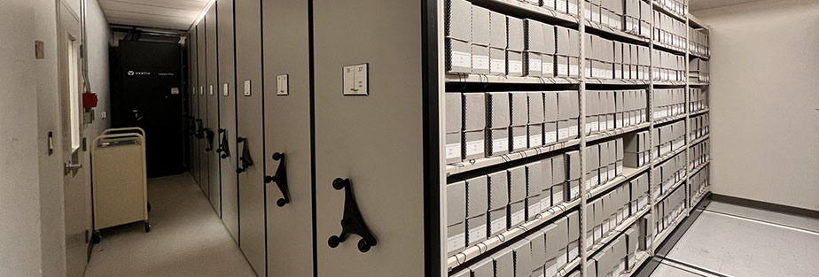 Compact shelving with grey boxes on the shelves and a book cart.