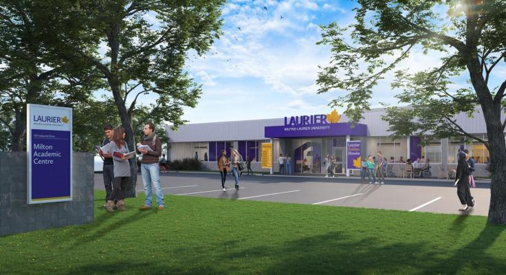 Exterior view the Laurier Milton Academic Centre. Image shows parking spots between trees on grassy area with trees and the entrance to the centre. No stairs to entrance.