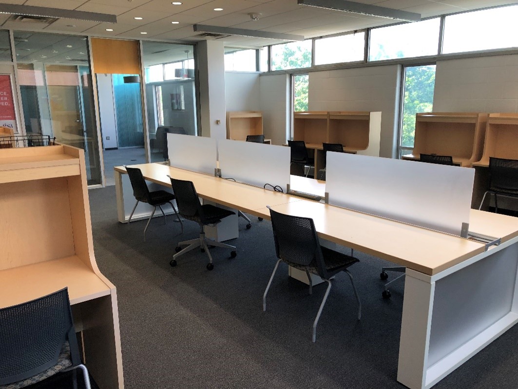 An area of the graduate commons. Individual desks around the room. In the middle is a long table with three chairs on either side.