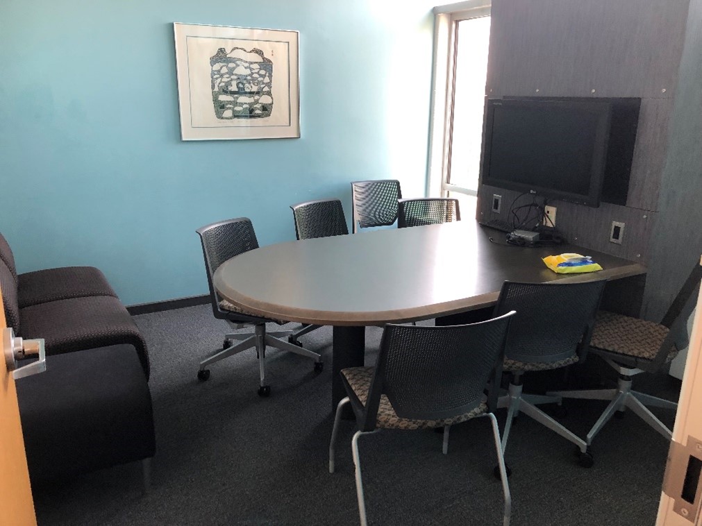 A group study room in the graduate commons. The are about seven chairs around a table. A computer monitor is on the wall