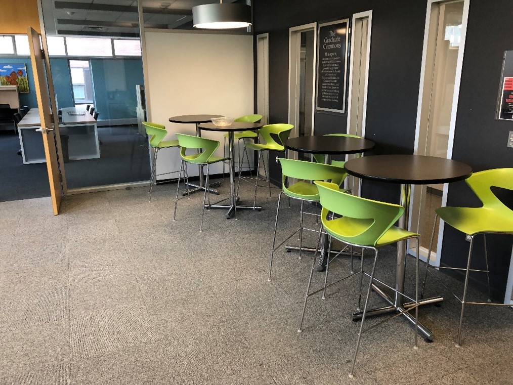 Another area of the graduate lounge. There are tall lounge chairs with round tables on one side of the room.