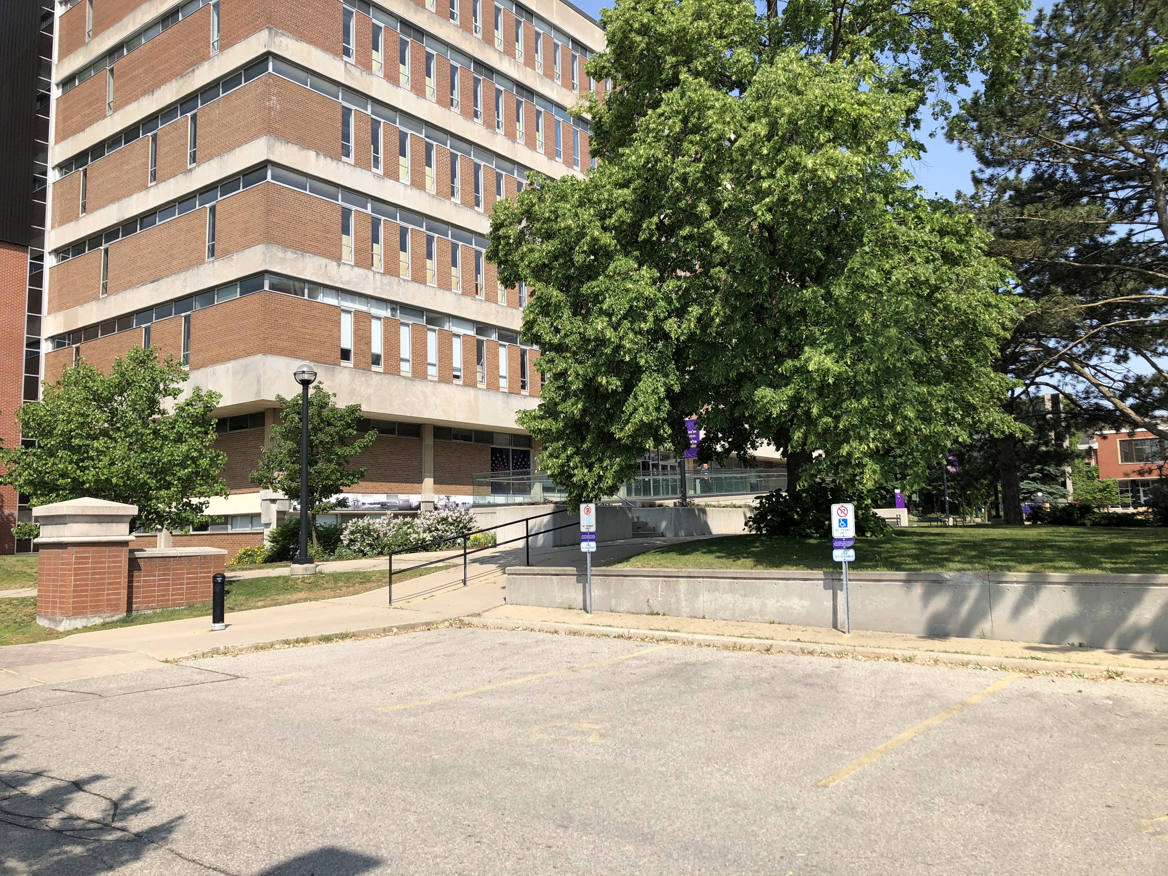 Parking spaces outside the library. Showing accessible parking spot. The route has a fixed bollard then a gentle slope with a handrail guiding up the middle.