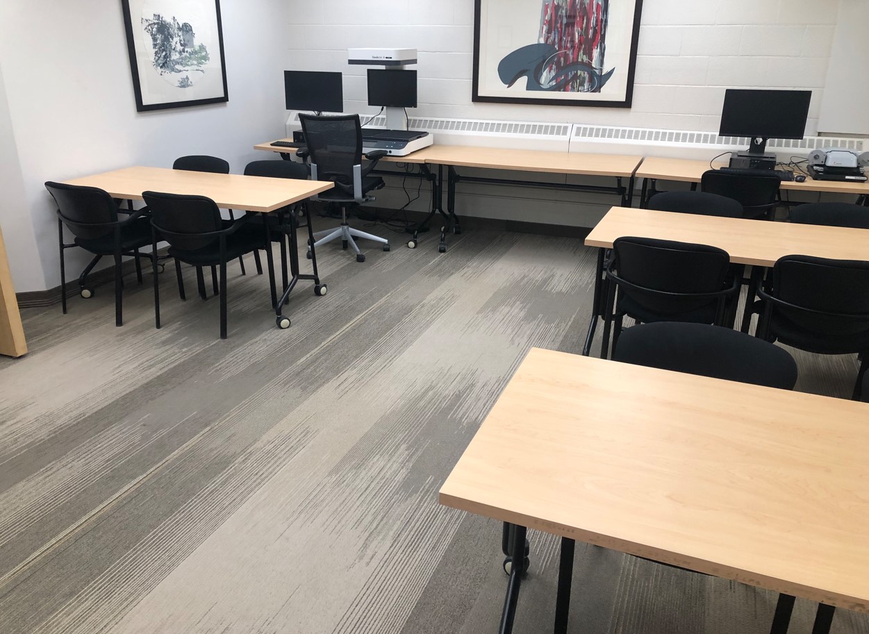 Tables on wheels, with four chairs with armrests around each. A micofilm reader and digital book scanner on a long table