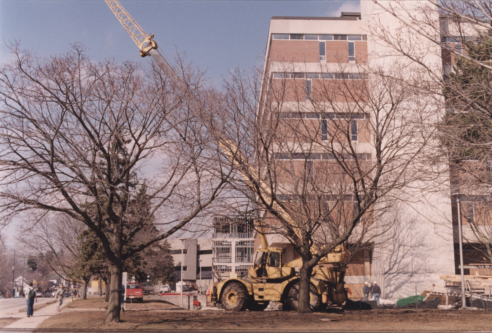 Exterior of Laurier Library building with construction vehicle and supplies in foreground, students walking by and other campus buildings in background