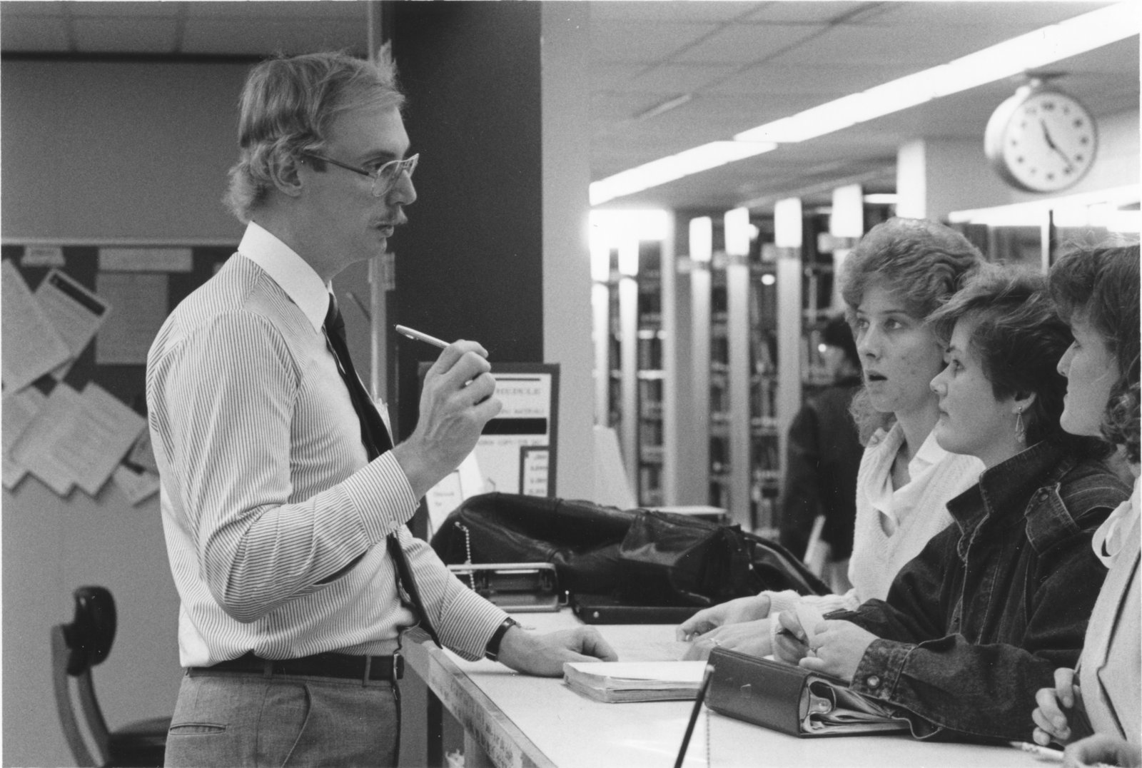Students at a counter with a staff member assisting them and bookshelves in the background