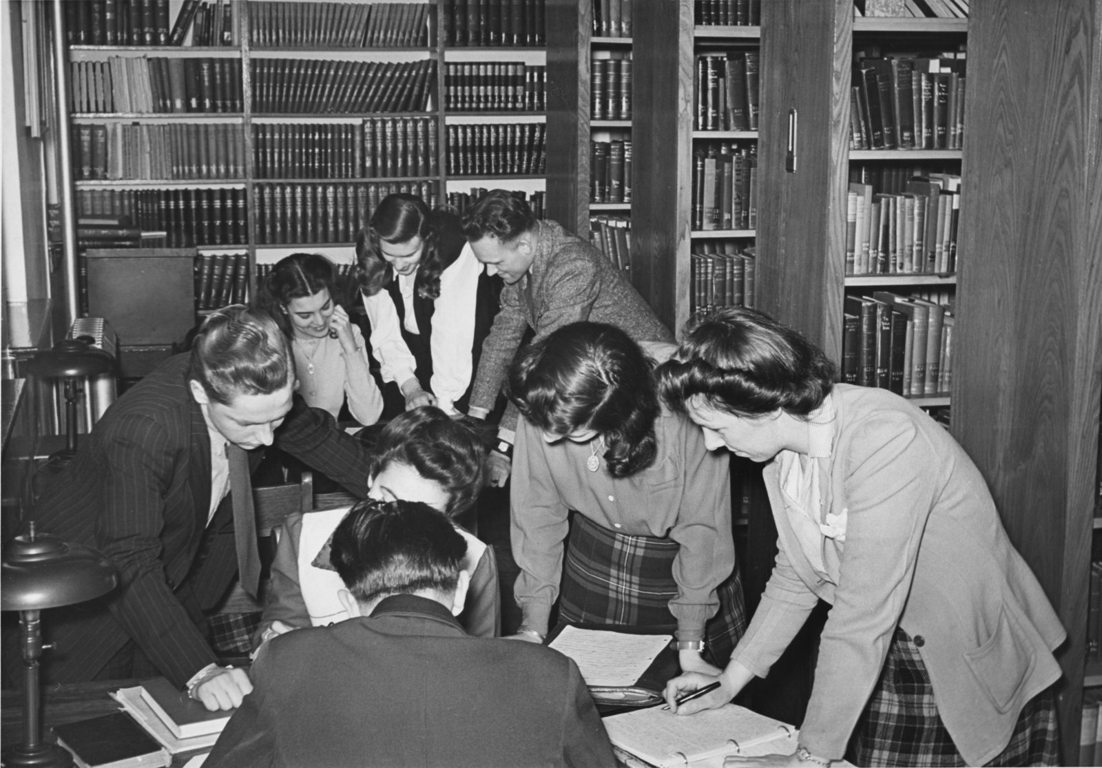 Students gathered around a table looking at notes with bookshelves in the background