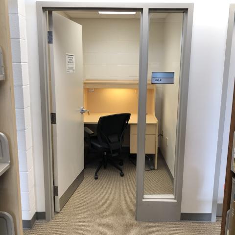 A private study room. There's a desk with large surface and chair. Braille on door signs