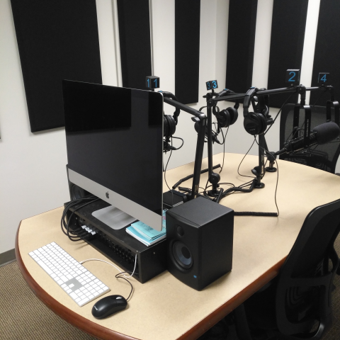 podcast studio desk with an iMac desktop, headsets, and three microphones on articulated arms.  Sound proofing is on the walls.